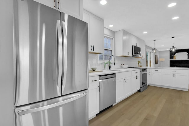 kitchen featuring tasteful backsplash, appliances with stainless steel finishes, light wood-style floors, white cabinets, and a sink