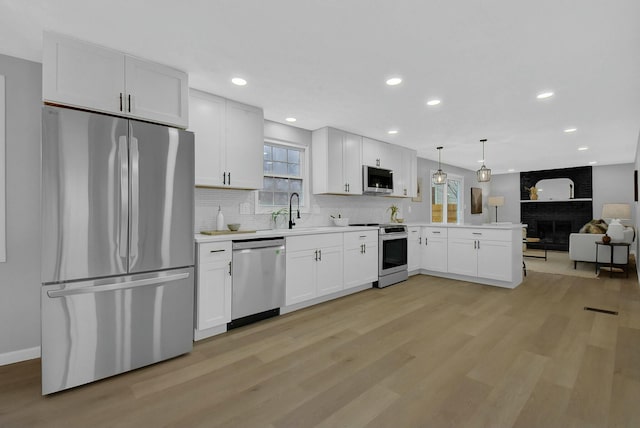 kitchen with stainless steel appliances, a peninsula, open floor plan, light wood-type flooring, and decorative backsplash