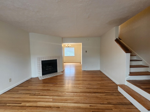 unfurnished living room featuring a textured ceiling, a tile fireplace, wood finished floors, baseboards, and stairs