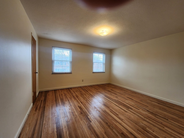 empty room featuring baseboards, a textured ceiling, and hardwood / wood-style floors