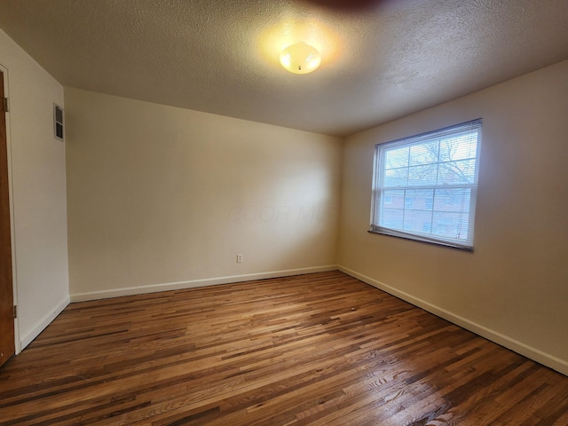 empty room featuring visible vents, a textured ceiling, baseboards, and wood finished floors