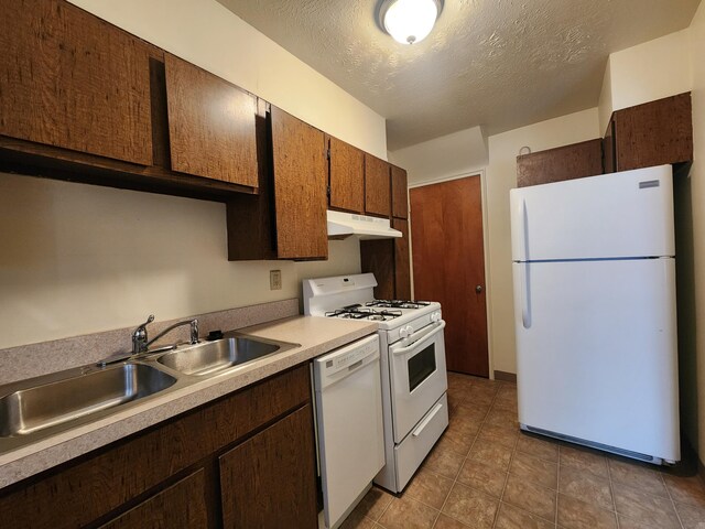 kitchen with white appliances, light countertops, a textured ceiling, under cabinet range hood, and a sink