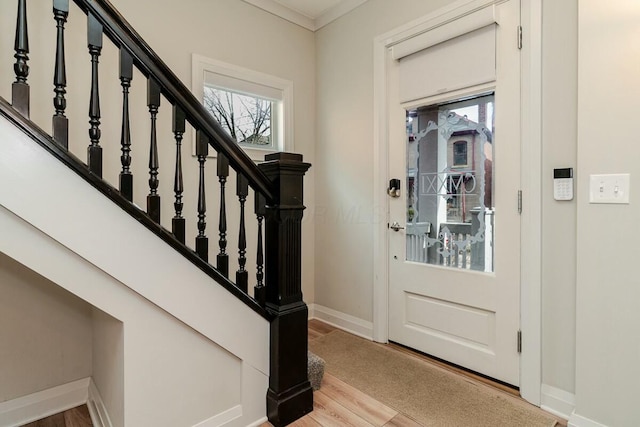 entryway with ornamental molding, wood finished floors, baseboards, and stairs