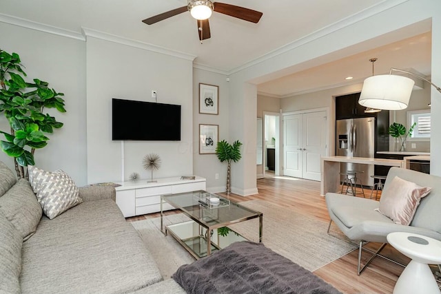 living room with crown molding, light wood-style flooring, baseboards, and ceiling fan