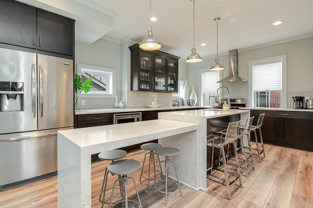 kitchen featuring light wood-type flooring, wall chimney exhaust hood, ornamental molding, and stainless steel fridge with ice dispenser