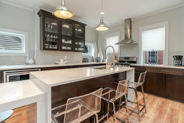 kitchen with beverage cooler, a sink, ornamental molding, wall chimney exhaust hood, and gas stove