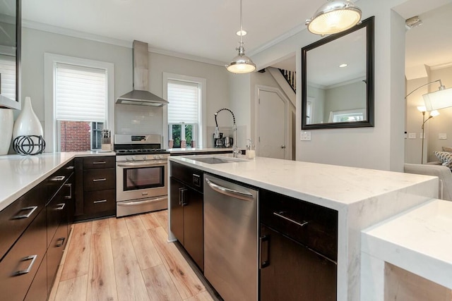 kitchen with wall chimney exhaust hood, ornamental molding, stainless steel appliances, light wood-style floors, and a sink