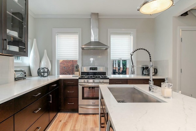 kitchen with a sink, ornamental molding, wall chimney range hood, light wood-type flooring, and gas stove