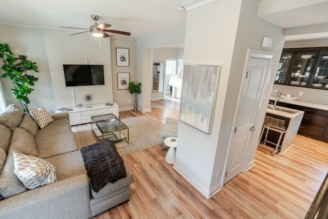 living area featuring a ceiling fan, crown molding, light wood-style flooring, and baseboards