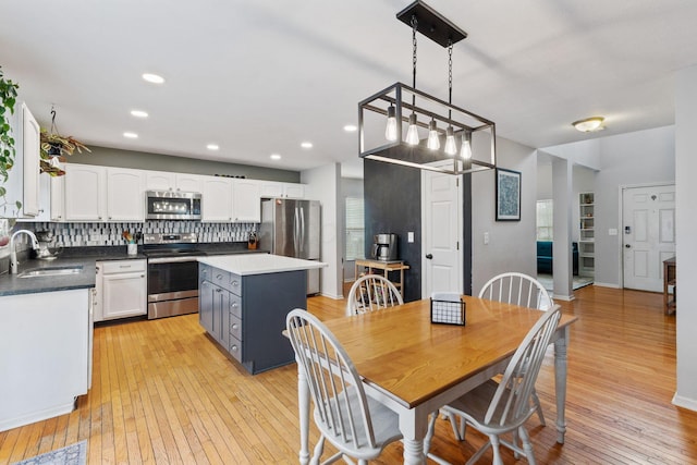 kitchen featuring tasteful backsplash, white cabinets, light wood-style flooring, stainless steel appliances, and a sink