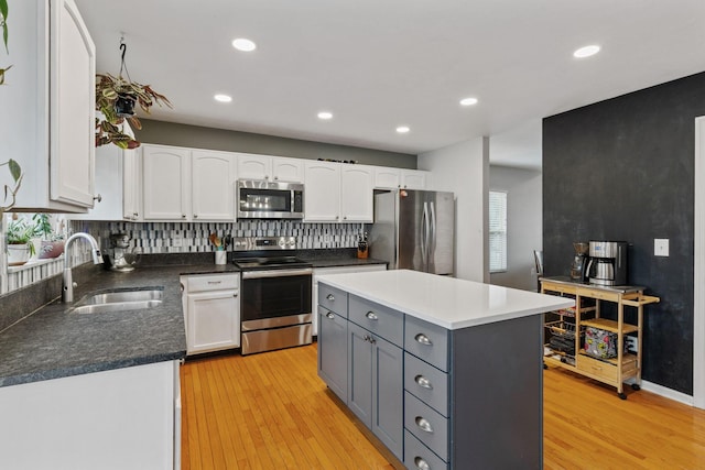 kitchen featuring appliances with stainless steel finishes, gray cabinetry, light wood-type flooring, white cabinetry, and a sink