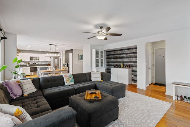 living room featuring light wood-style floors, baseboards, and ceiling fan with notable chandelier