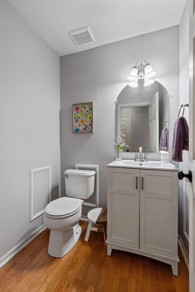 half bathroom with wood-type flooring, visible vents, vanity, and toilet