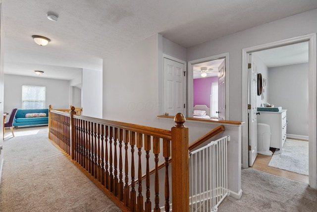 hall with a textured ceiling, carpet flooring, and an upstairs landing