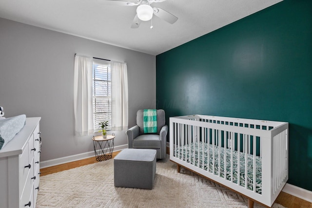 bedroom featuring light wood-type flooring, a nursery area, ceiling fan, and baseboards