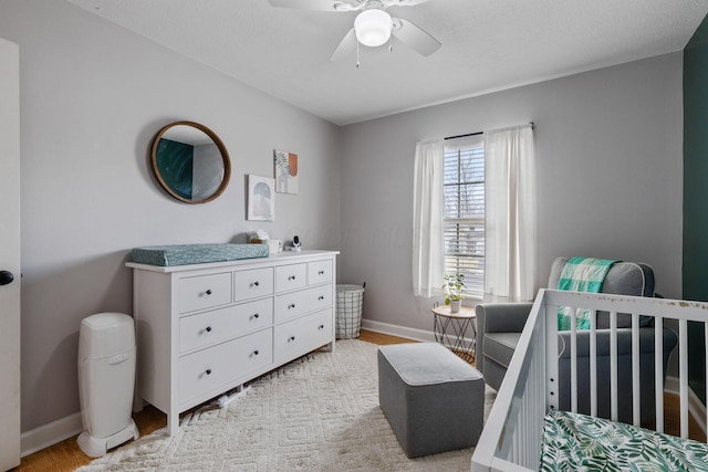 bedroom with a nursery area, baseboards, light wood finished floors, and a ceiling fan