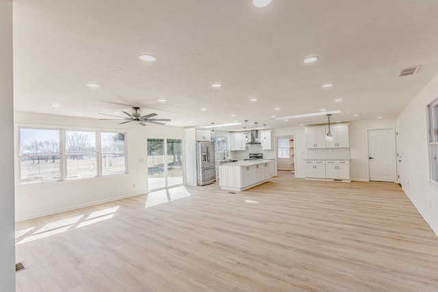 unfurnished living room with light wood-type flooring, a sink, visible vents, and baseboards