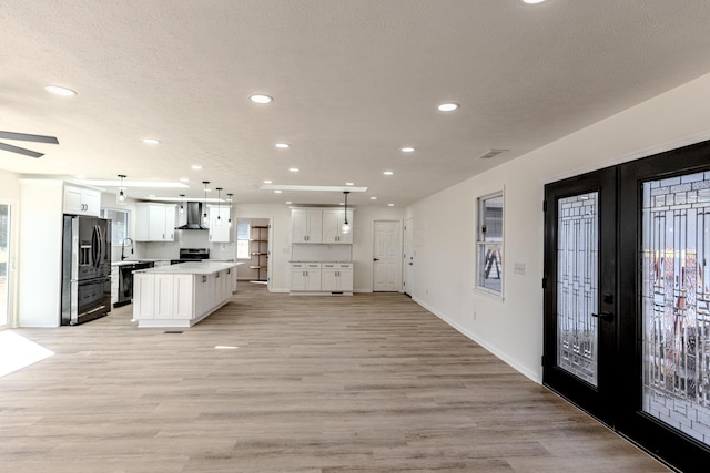 kitchen featuring french doors, open floor plan, white cabinetry, wall chimney range hood, and black appliances