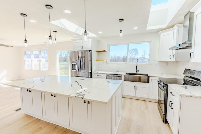 kitchen featuring tasteful backsplash, light wood-style flooring, appliances with stainless steel finishes, a kitchen island, and wall chimney exhaust hood