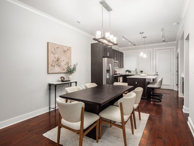 dining space with dark wood-style flooring, rail lighting, an inviting chandelier, ornamental molding, and baseboards