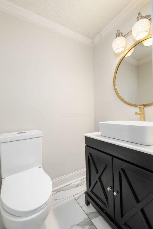 half bath with marble finish floor, toilet, ornamental molding, vanity, and baseboards