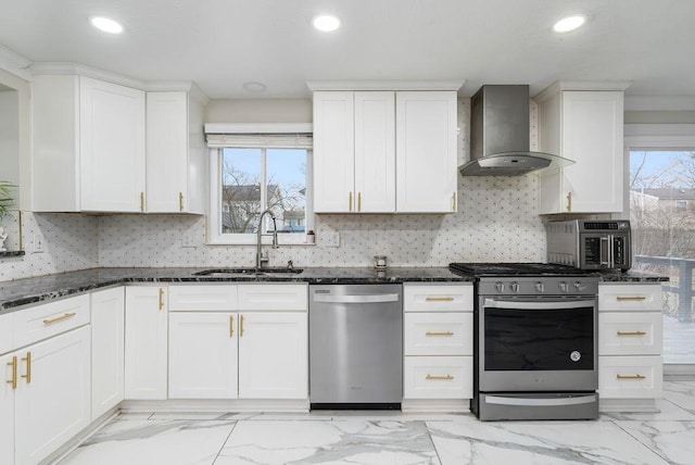 kitchen featuring stainless steel appliances, white cabinetry, a sink, wall chimney range hood, and dark stone counters