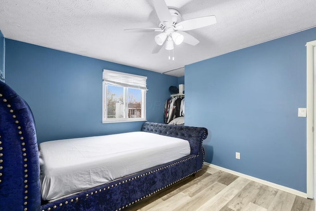 bedroom featuring ceiling fan, a textured ceiling, baseboards, and wood finished floors