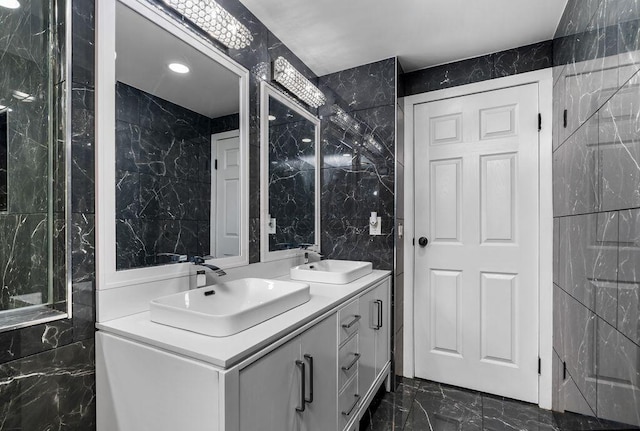 full bathroom with marble finish floor, double vanity, a sink, and tile walls