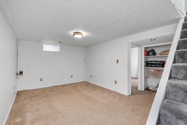 below grade area with light colored carpet, a textured ceiling, baseboards, and stairs