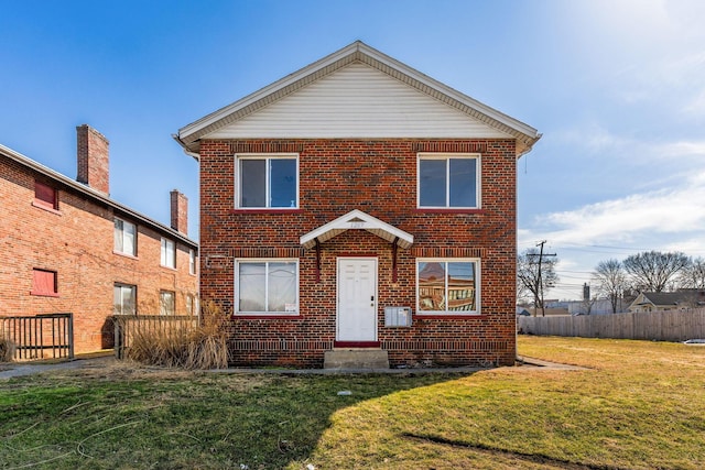 traditional-style house featuring a front yard, brick siding, and fence