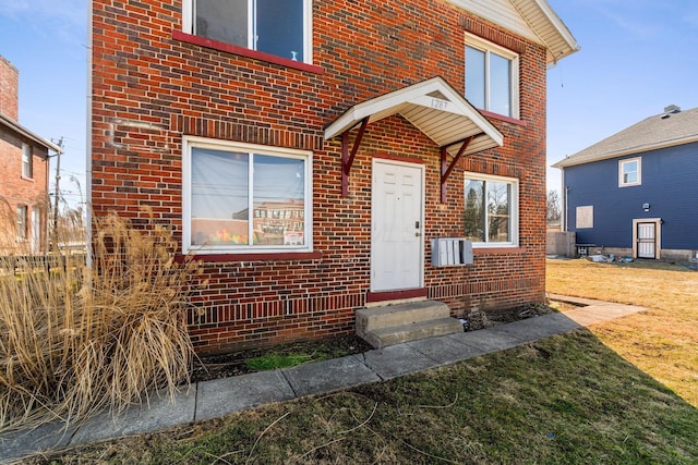 view of exterior entry with cooling unit, a lawn, and brick siding