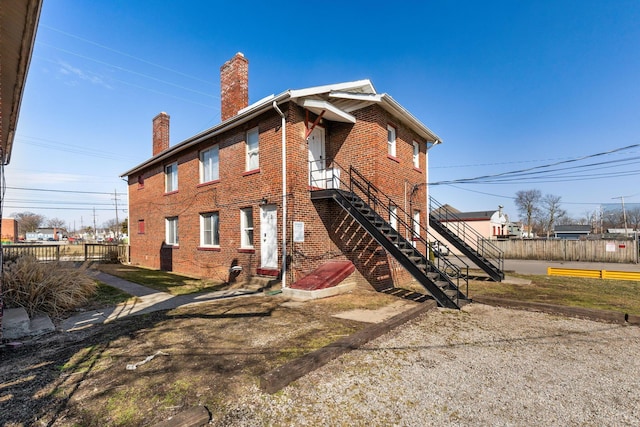 back of house with entry steps, brick siding, a chimney, and fence