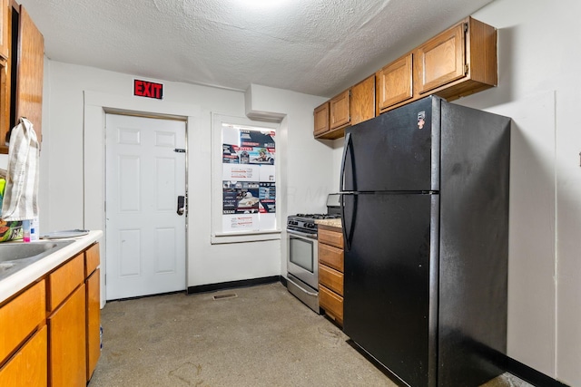 kitchen featuring a textured ceiling, light countertops, freestanding refrigerator, brown cabinetry, and stainless steel range with gas stovetop