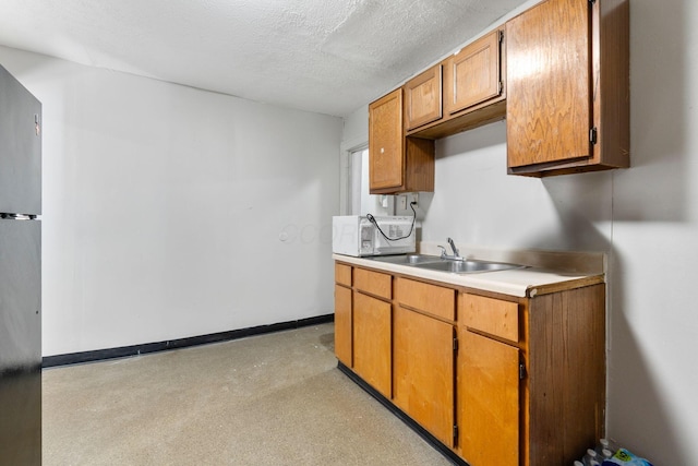 kitchen featuring light countertops, white microwave, a sink, a textured ceiling, and baseboards