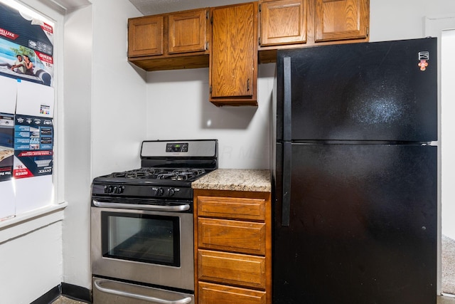 kitchen with light countertops, brown cabinetry, stainless steel range with gas stovetop, and freestanding refrigerator