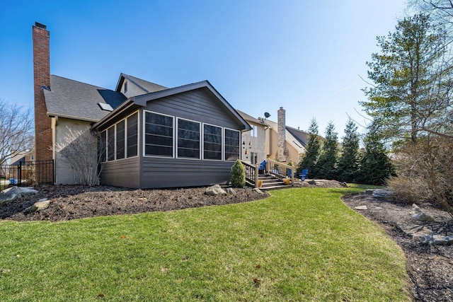 rear view of house featuring a chimney, a yard, and a sunroom