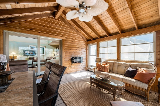 living room with ceiling fan, a multi sided fireplace, wood walls, lofted ceiling with beams, and wooden ceiling