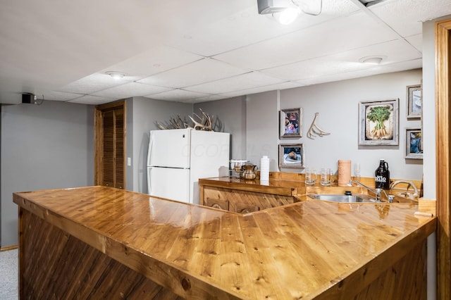 kitchen featuring butcher block countertops, freestanding refrigerator, a paneled ceiling, and a sink