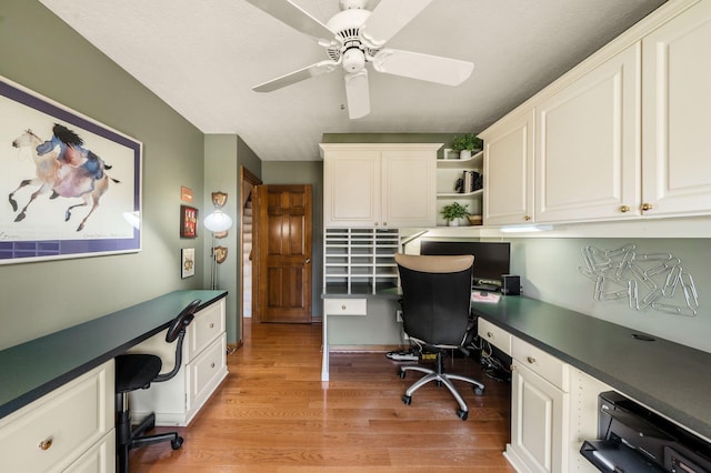 office area with a ceiling fan, built in desk, and light wood finished floors