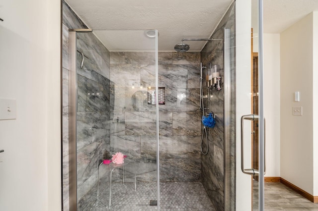 full bathroom featuring a shower stall, a textured ceiling, baseboards, and wood finished floors