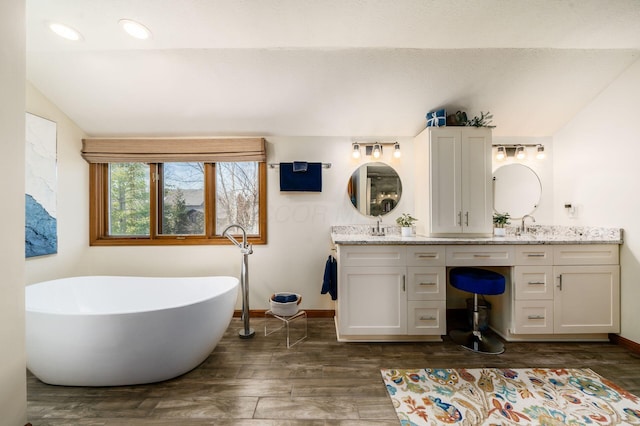 full bath featuring baseboards, double vanity, vaulted ceiling, wood finished floors, and a soaking tub