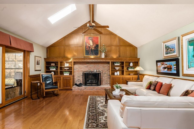 living area featuring light wood-style flooring, wood walls, a brick fireplace, ceiling fan, and vaulted ceiling with beams