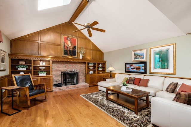 living room with light wood-type flooring, beam ceiling, a ceiling fan, a skylight, and a brick fireplace