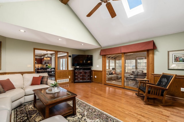 living room featuring light wood finished floors, wainscoting, ceiling fan with notable chandelier, and a healthy amount of sunlight