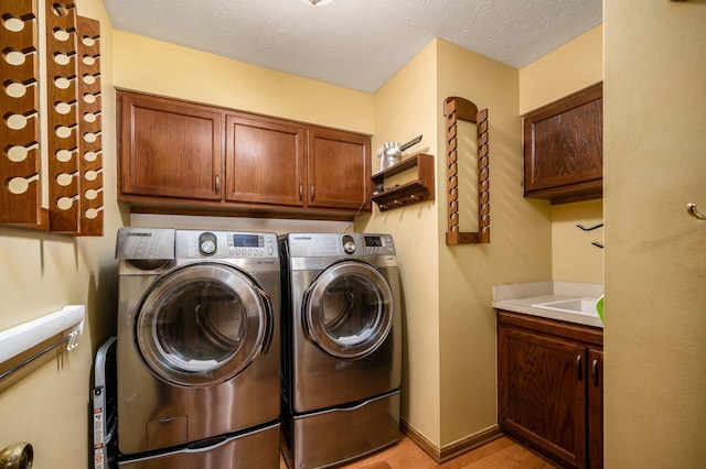 clothes washing area featuring light wood-type flooring, a textured ceiling, cabinet space, baseboards, and washing machine and clothes dryer