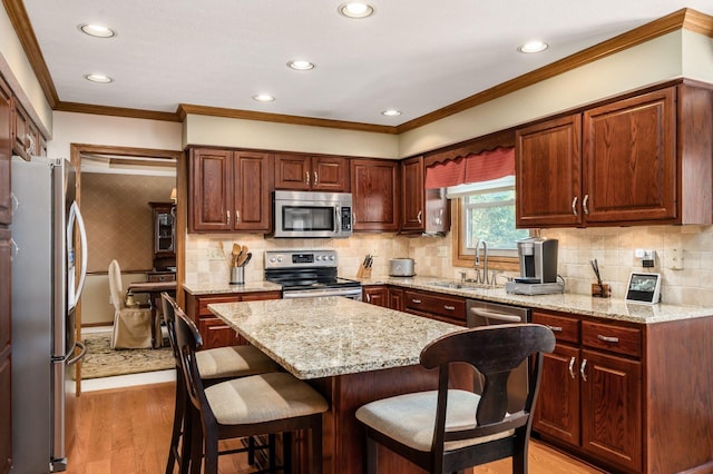 kitchen featuring a kitchen bar, light wood-type flooring, a sink, light stone counters, and stainless steel appliances