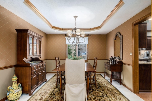 dining space featuring baseboards, wallpapered walls, ornamental molding, a raised ceiling, and a chandelier