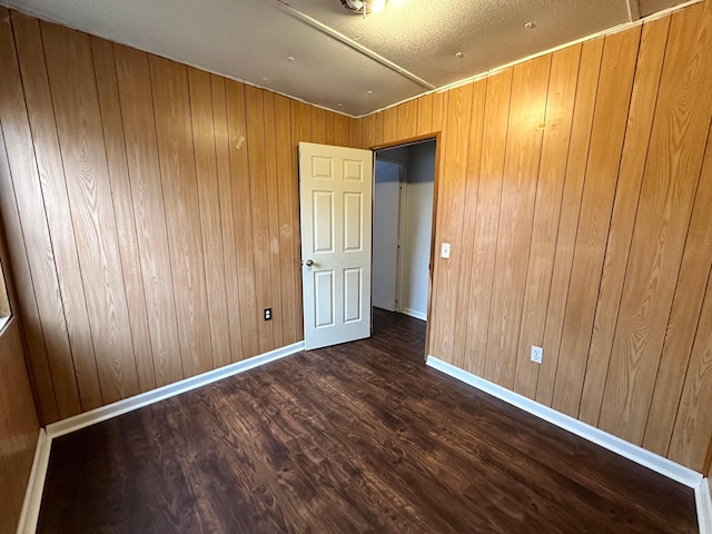 empty room featuring wooden walls, baseboards, and wood finished floors