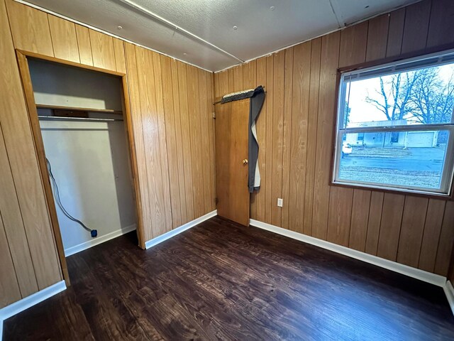 unfurnished bedroom featuring dark wood-type flooring, a closet, wood walls, and baseboards