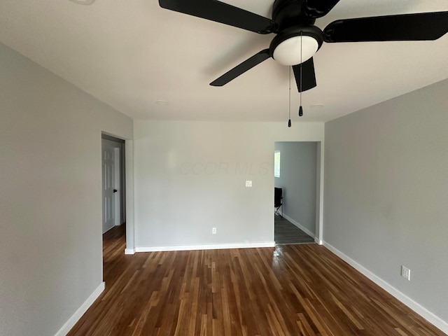 unfurnished room with dark wood-type flooring, a ceiling fan, and baseboards